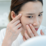 鏡を見ながら目元や頬の小さな変化を気にしている女性。