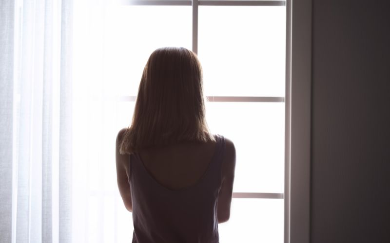 窓際に立って何かを思う女性の後ろ姿の画像。