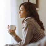 窓辺で静かに考えごとをする女性。心の声に耳を傾けている様子